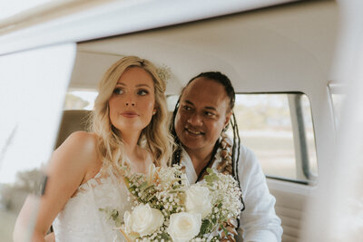 A candid and creative wedding photo of a bride and groom looking through the window of the kombi van