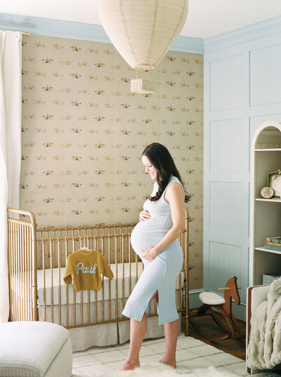 Brunette pregnant woman dressed in white lays on white bed at Little Rock studio holding pregnant belly photographed by Bailey Feeler
