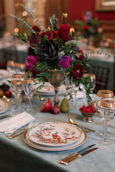 A fall place setting  with rich colors of purple, red, and magenta  on a  blue tablecloth