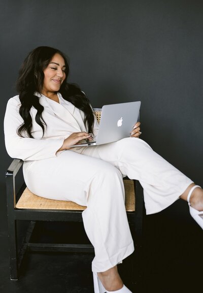 Women sitting on a chair, looking at laptop, wearing light pant suit