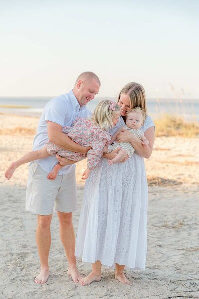 Dad airplanes toddler girl into mom and baby brother for laughs during their beach family session in Hilton Head, SC with Hilton Head Photographer, Lamp and Light Photography.