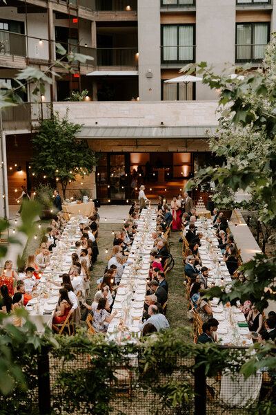 Kelly and Michael Lugo's wedding reception as photographed from a tall balcony with lush greenery, showing long tables with guests gathered for dinner