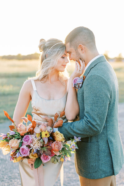 Bride and groom posing with their heads together while she holds a colorful flower bouquet