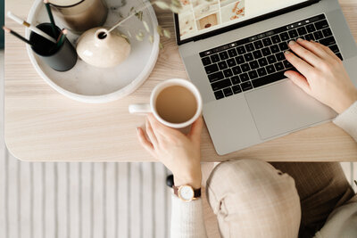 A cozy workspace scene featuring a woman holding a coffee mug at a light wood desk with a laptop, vase, and mood board in view. Beside it, a quote reads: “Balance over burnout. Work should support the life you love, not steal it from you.” This visual emphasizes Catherine Shuman’s belief in operations consulting that protects mental clarity for women in architecture and interior design.
