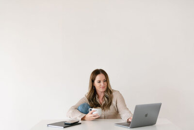Woman looking at her laptop and holding a cup of coffee