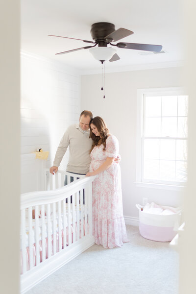 An in home newborn session featuring a mother and father leaning in looking down at their baby girl in her crib by Northern Virginia Newborn Photographer