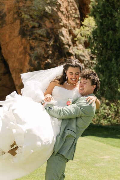 Groom lifting bride joyfully during their first look outdoors in the Colorado mountains 