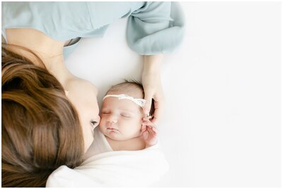 mom laying opposite of baby girl, kissing her on cheek.
