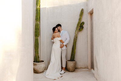 Bride and groom share an intimate moment framed by tall cacti at a minimalist Tulum Airbnb wedding venue.