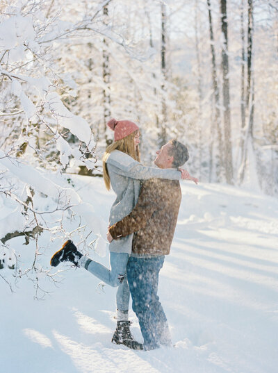 couple jumping on each other with snow falling in winter wonderland