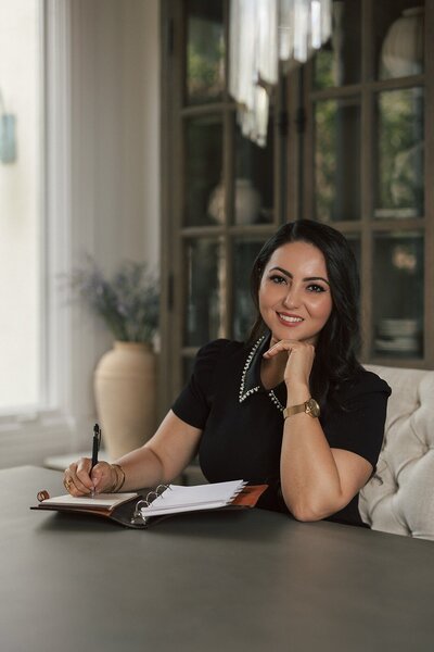 A headshot of the owner sitting at the table writing in her notebook.