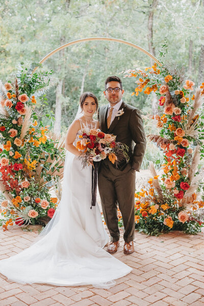 Bride and groom framed by terracotta and orange floral arch, showcasing Bloom Bar’s bold wedding floral arrangements in Central Texas.