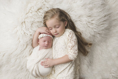 a baby and her sister laying on a fur white backdrop