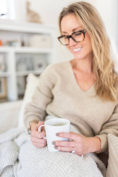 Branding photo of woman sitting on the couch holding a white cup on her legs.