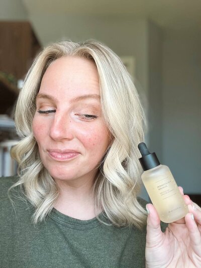 Kelsey Hansen wearing a green t-shirt as she smiles and looks down at the Dermatology Serum EX