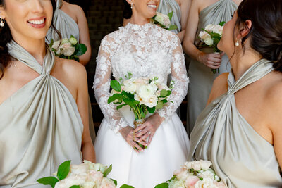 woman in lace white dress surrounded by women in silk taupe dresses all holding flowers