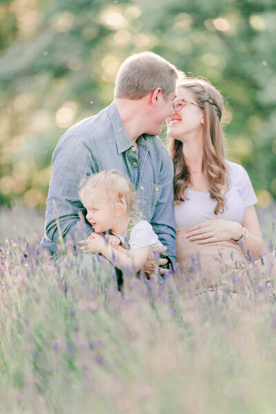 Parents holding newborn baby in white knotted onesie and smiling, dad kissing baby's head by NH family photographer Fieldstone Studio