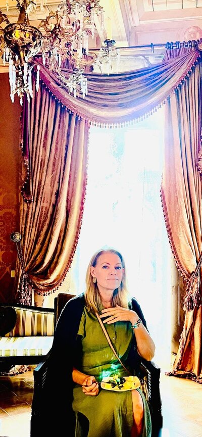 Casa Erica founder Heather sitting in an ornately decorated room, in front of a draped curtain.