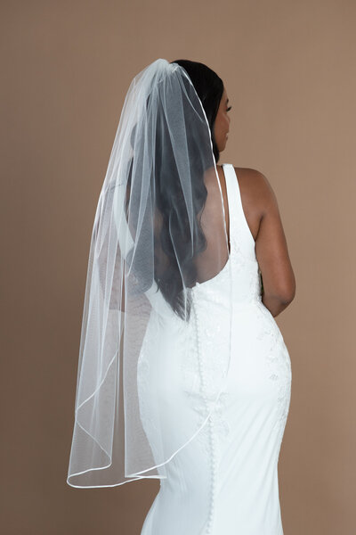 Bride wearing a fingertip length veil with small ribbon edge and holding a white and black bouquet