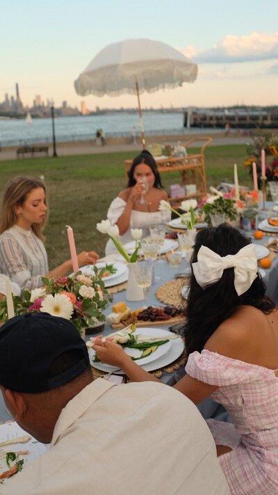 Guests enjoying an elegant outdoor dinner picnic with floral centerpieces, candles, and waterfront views, styled by Yours Truly, a wedding planner and designer in New Jersey.