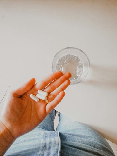 A hand holding supplements with a glass of water behind her hand. 