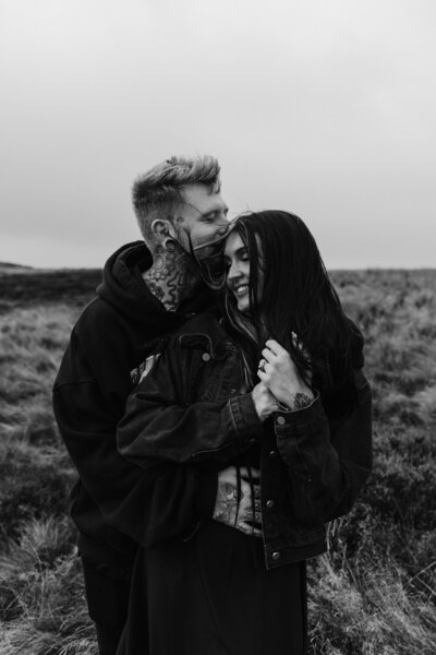 Black and white shot of a cool couple poses confidently next to a motorbike, epitomising their alternative and stylish approach to love and life at Willow Marsh Farm