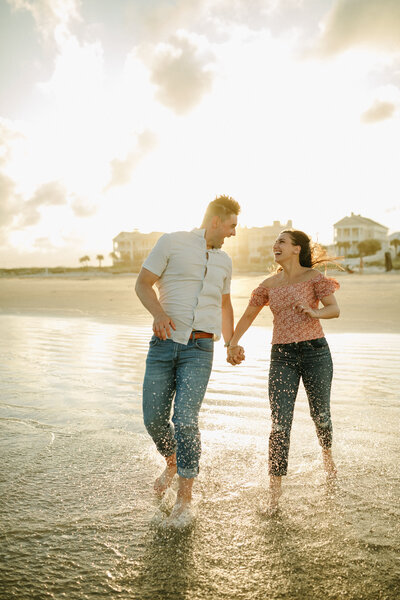 man and woman holding hands and smiling at each other while walking on the beach