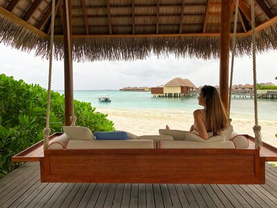 Overwater bungalow in the Maldives with beachfront daybed and tranquil sea views.