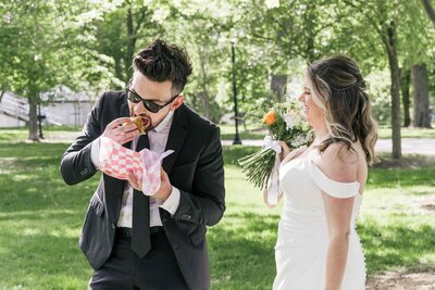 Groom eating a Chicago dog while bride laughs at him