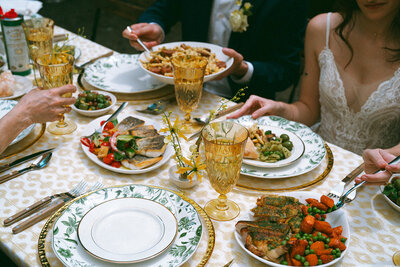 Colorful table spread at outdoor wedding in Brooklyn, NY featuring vibrant food, patterned plates and table cloth and detailed amber-colored glasses.