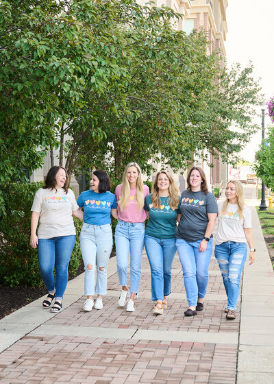 a team of women walking and laughing on sidewalk with shirts that say mama