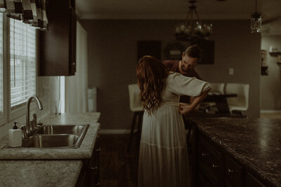 Husband fixing wife's dress in their home during their maternity session.