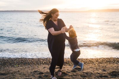 Playful maternity photo of mother and child spinning on Seattle beach