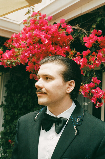 Stylish groom stands on a rooftop terrace with the New York City skyline behind him, just moments before the first look