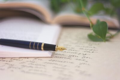 a fountain pen laying on top of a notebook and pieces of paper with writing on them