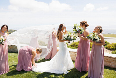 bridesmaids help bride with veil as it flies in the wind