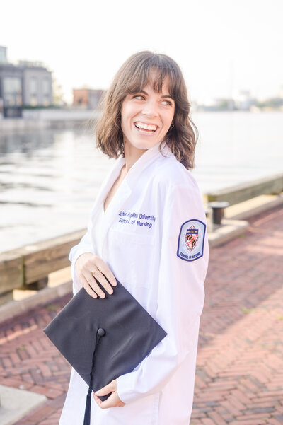 Nursing school grad smiles on the harbor during graduation session in Baltimore, MD