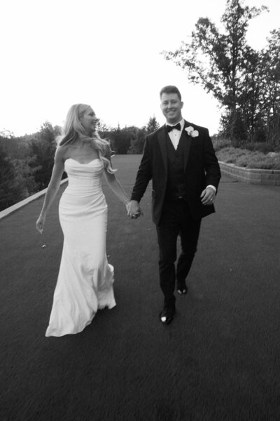 Bride and groom walking hand in hand outdoors, black-and-white photo.