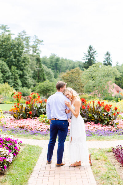 blonde haired girl holding onto her fiance in front of colorful gardens at Biltmore Estate for engagement session
