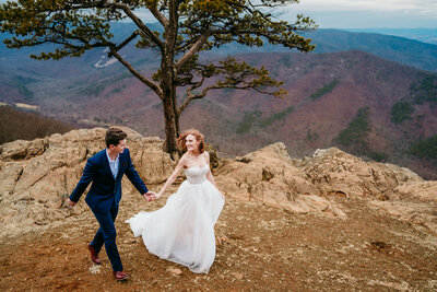 Bride and groom standing on a rocky cliff under a pine tree with mountain views in Blue Ridge Parkway during their adventurous elopement.