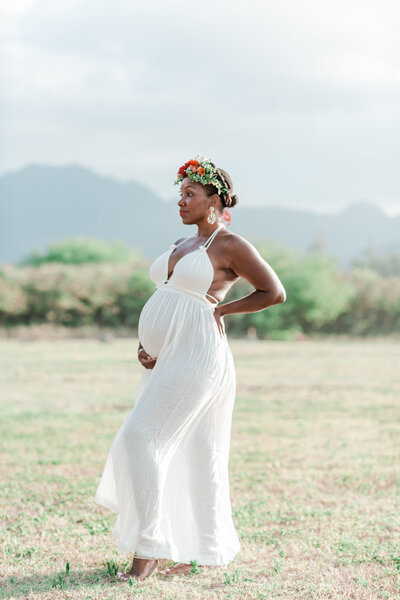Pregnant woman of color standing like a goddess  in a white dress in front of the Koolau Mountain range