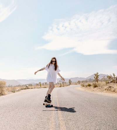 girl in white dress on skateboard at joshua tree in california by portrait photographer sabrina leigh photography