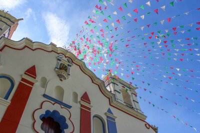 Colorful papel picado banners fluttering above a white and red church façade near Oaxaca ©Stephanie Dosch | theViatrix Private Mexico Luxury Travel