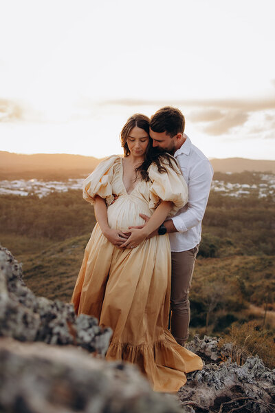 pregnant couple holding each other standing on rocks