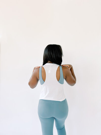 Woman wearing a white tank with a blue sports bra and blue leggings