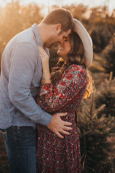 Engagement photo session with couple kissing in front of christmas tree farm