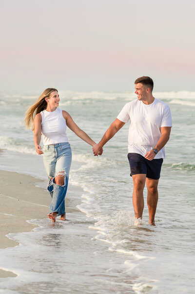 A man and woman holding hands while walking down the beach in Ocean City NJ during their engagement session