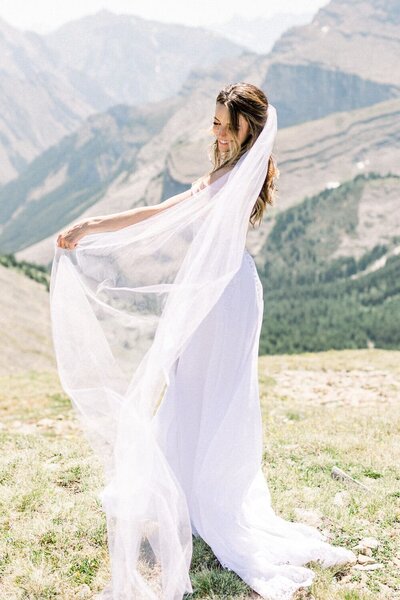 Capture the joyful moment of a bride playing with her veil on top of a mountain after landing in a helicopter. A stunning portrait of elegance and adventure set against the breathtaking backdrop of the Canadian Rockies.