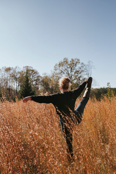 Alex Paige holding one leg in the air in a yoga pose in a grassy field