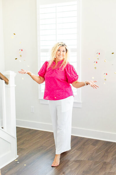 senior photographer in pink blouse and white pants throwing confetti up